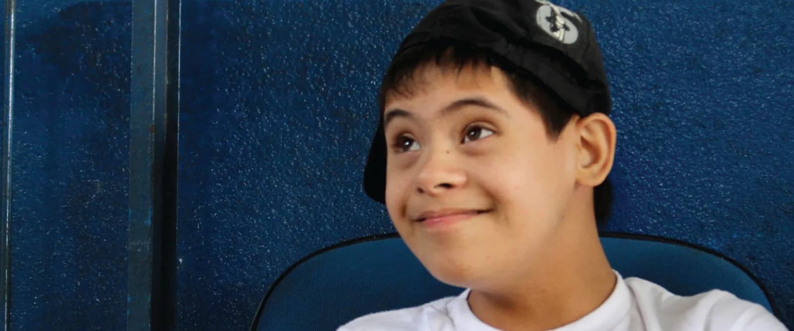 A smiling boy with Down syndrome wearing a cap